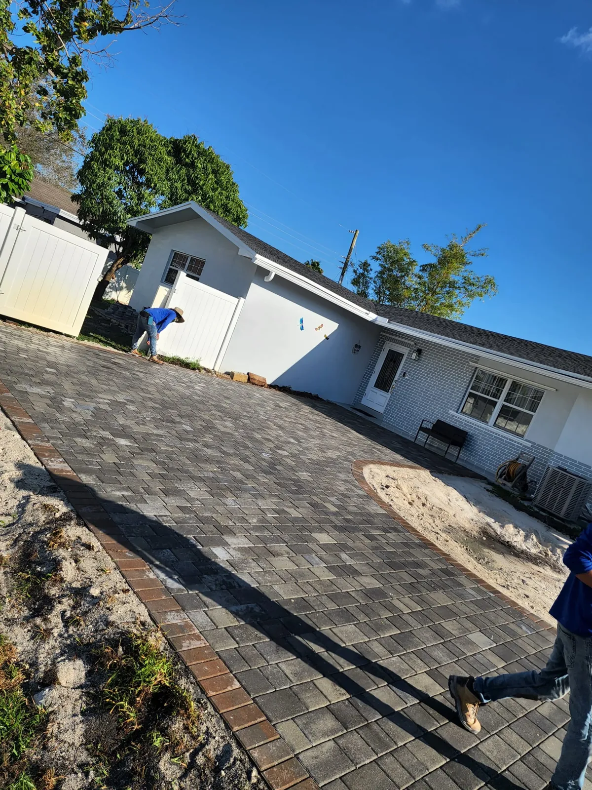 Dark gray pavers with a brick-toned border being laid along the side of a house