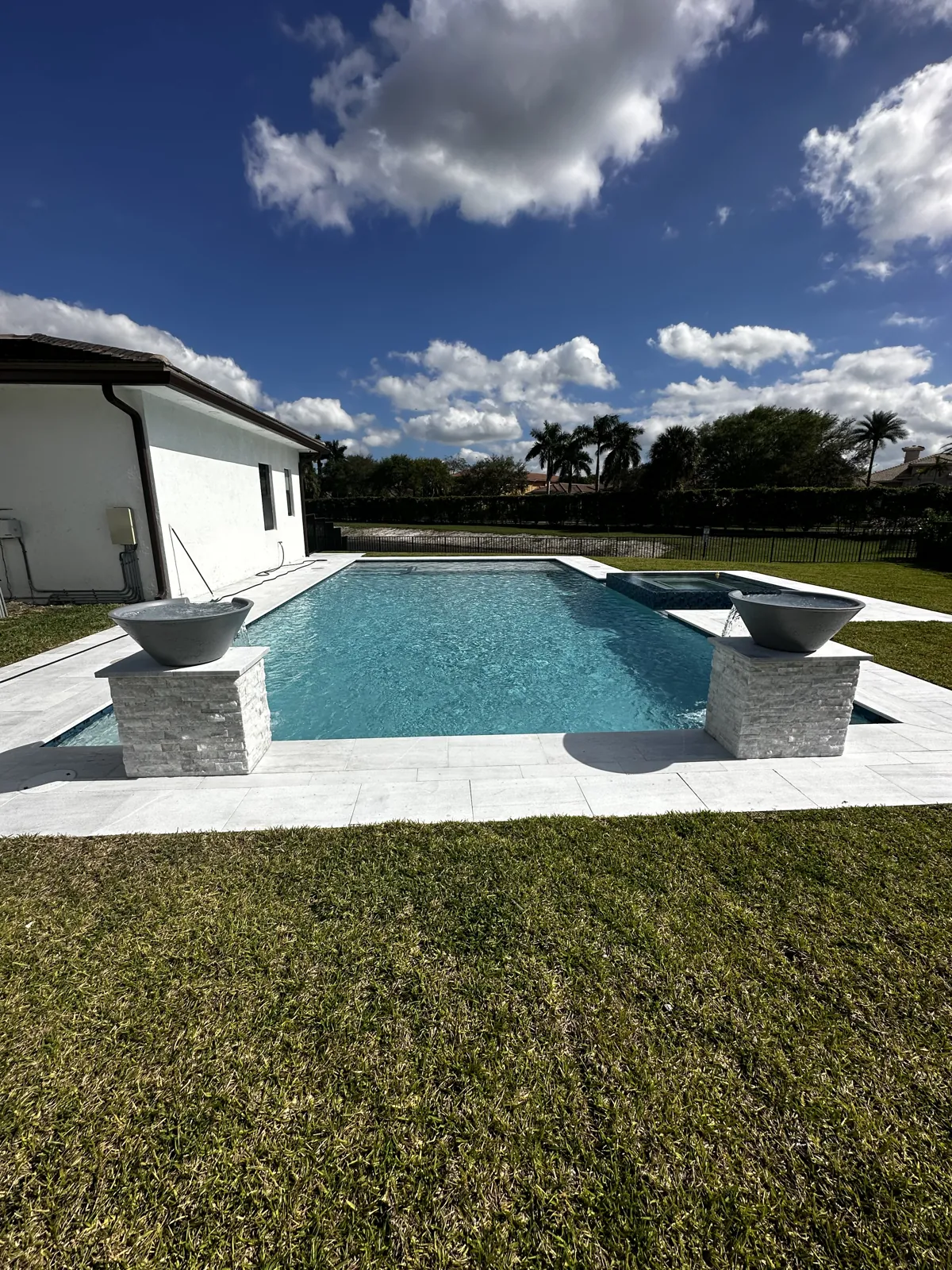 Pool with two stone-clad raised bowls and a pale deck edge beside a lawn