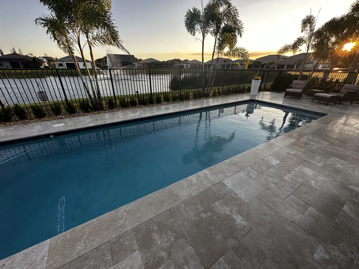 Gray-brown stone pool deck beside an iron fence in evening light
