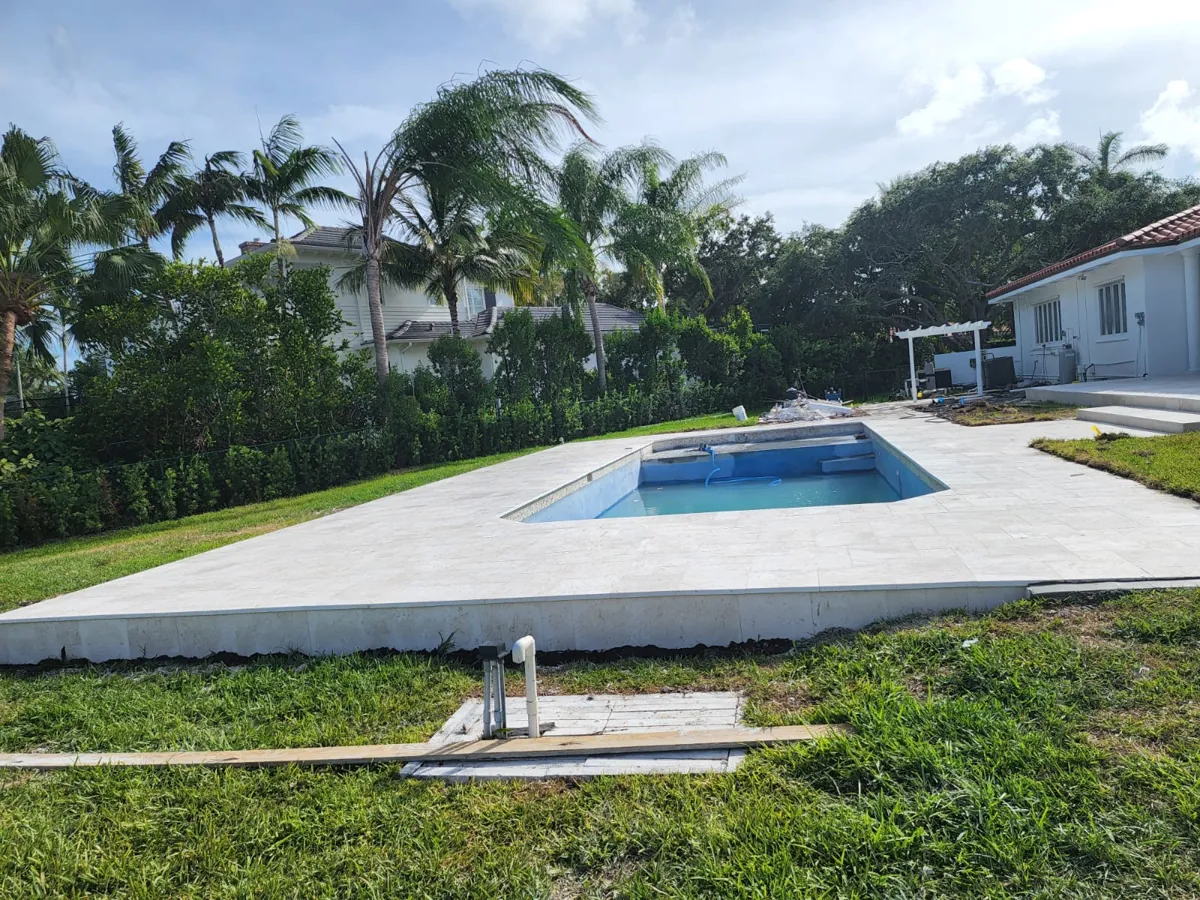 Pale paved pool edge across a lawn with a house and palms behind