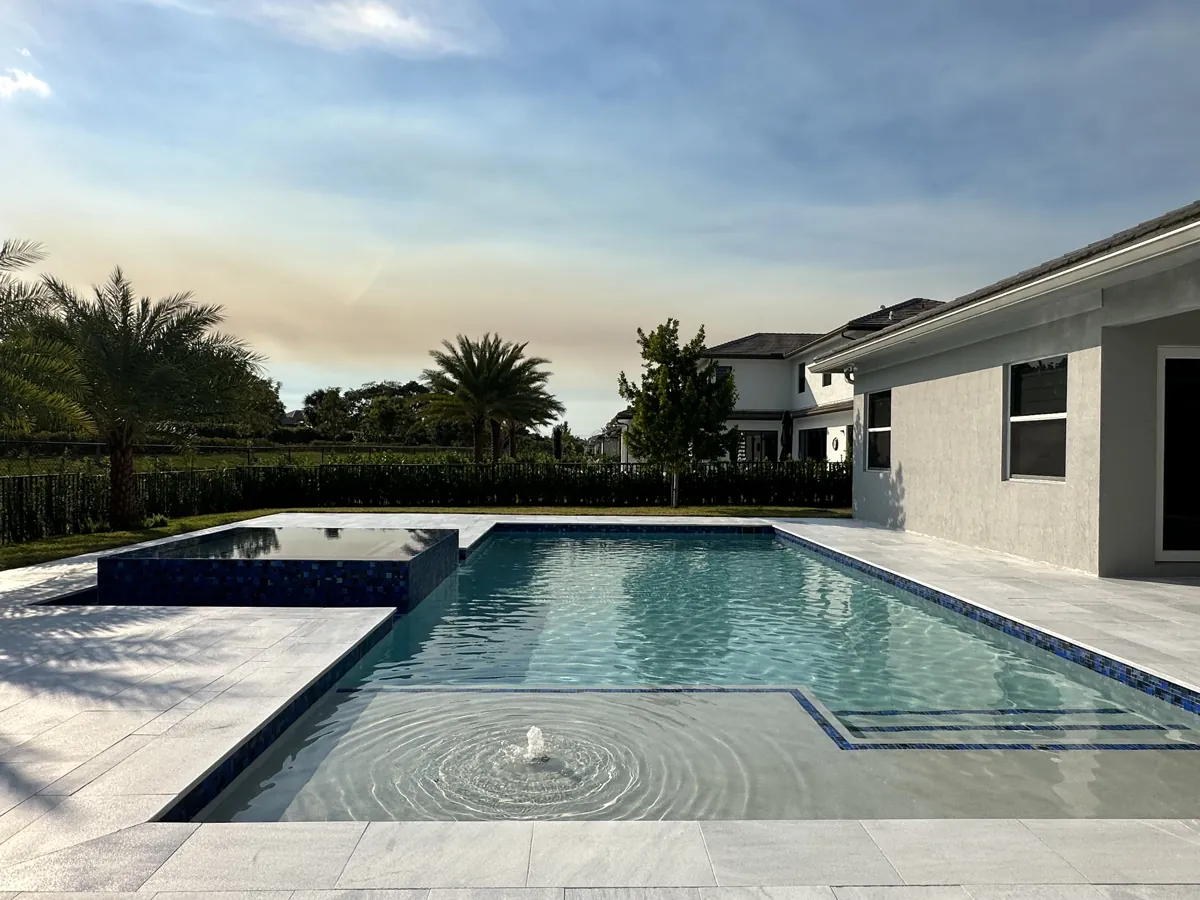 Pool at dusk with a fountain jet and a gray paved surround