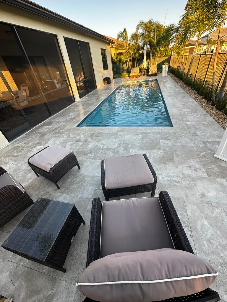 Narrow pool beside a screened lanai with a gray stone deck and outdoor seating