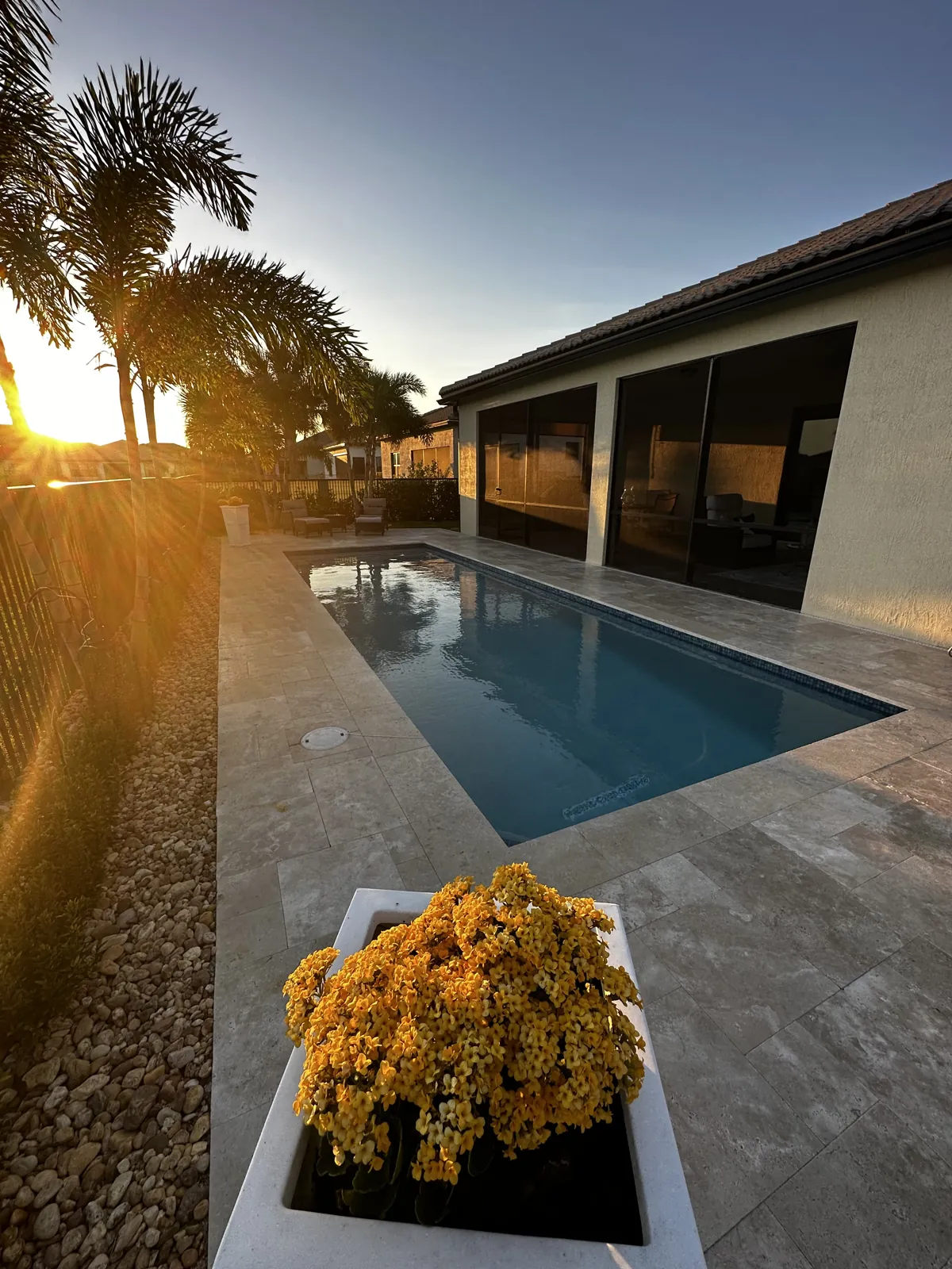 Narrow pool and stone deck beside a screened lanai in sunset light