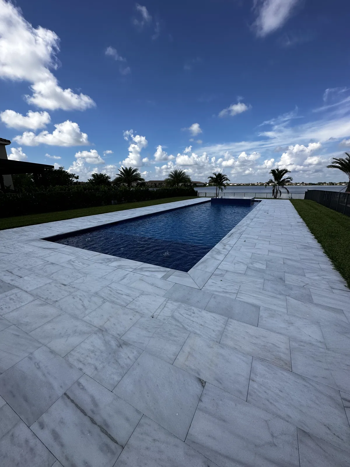 Long pool edge framed by large pale stone pavers beside a lawn