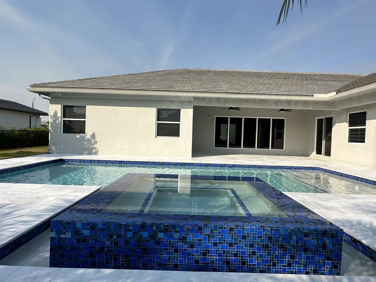 Raised spa faced in blue mosaic tile beside a pale stone pool deck