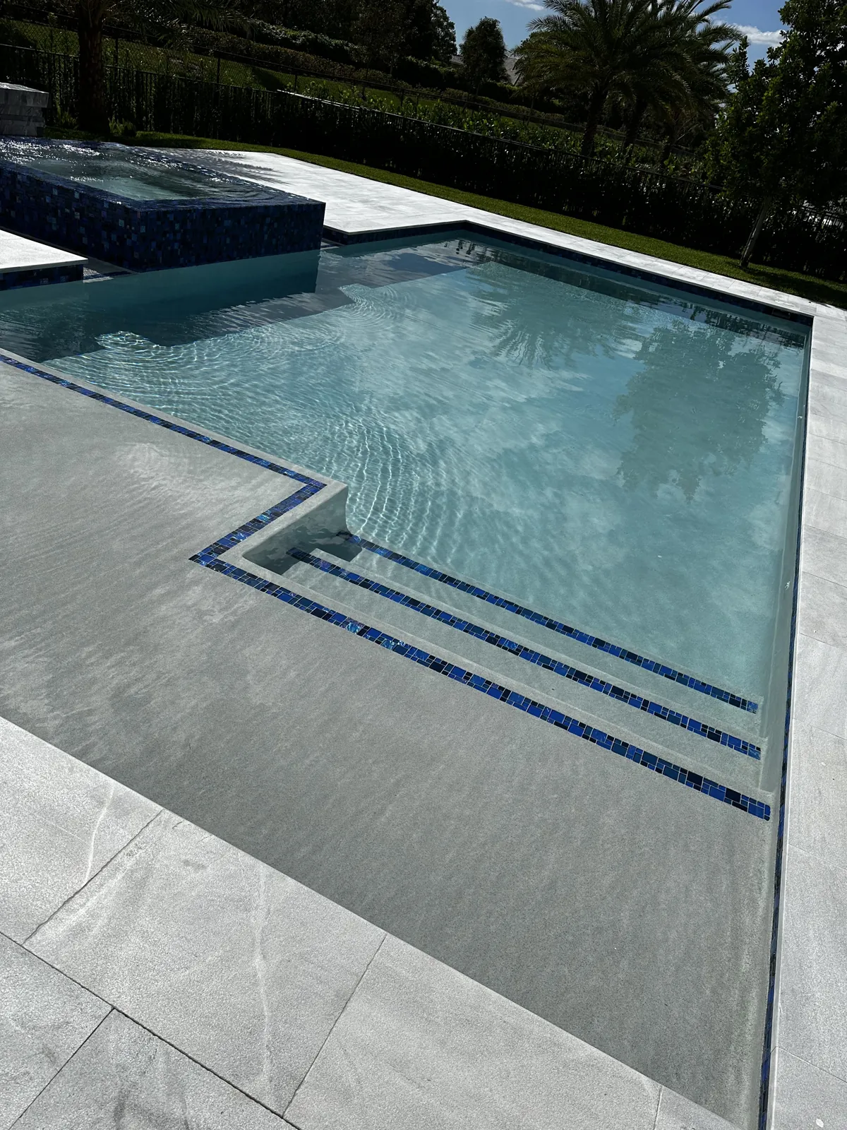 Pool steps trimmed with blue tile lines beside a gray tile deck