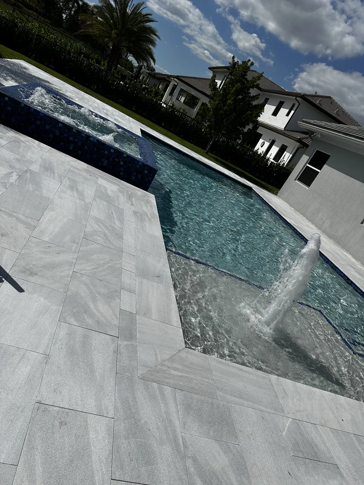 Pool water feature spilling into the pool beside a gray-white paved deck