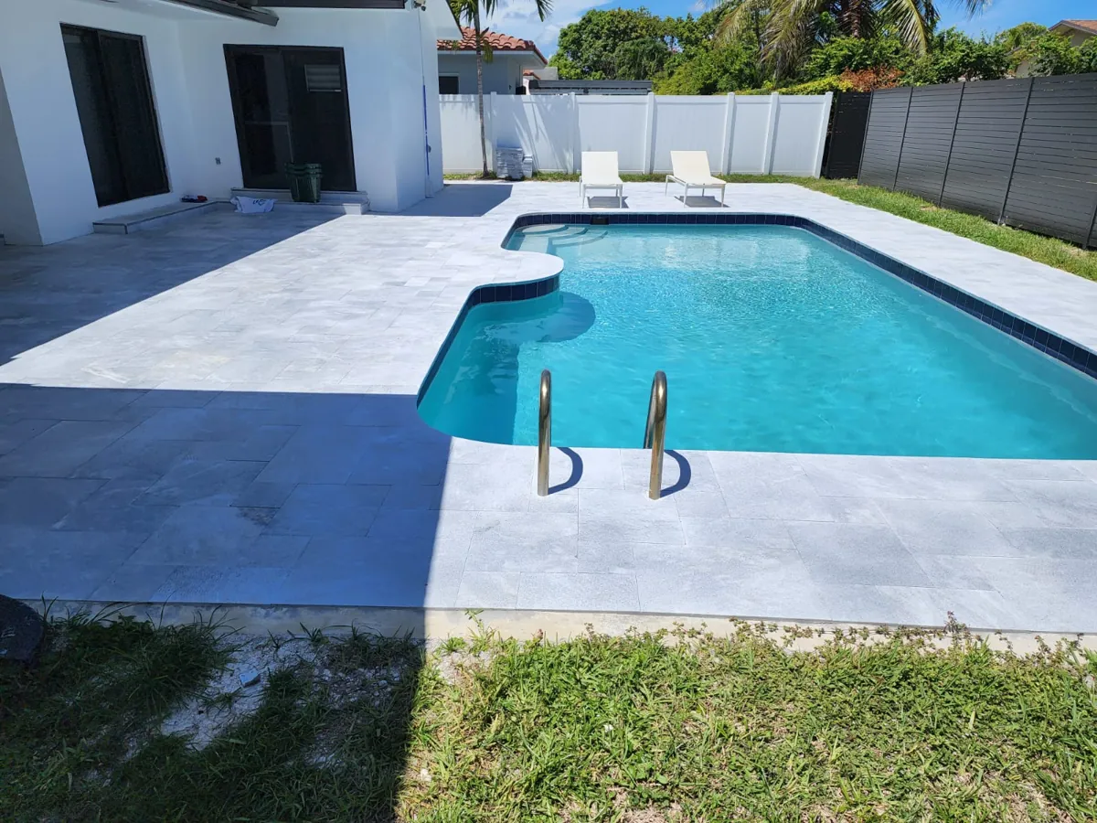 Pool with a white and gray stone deck, handrails and a strip of turf