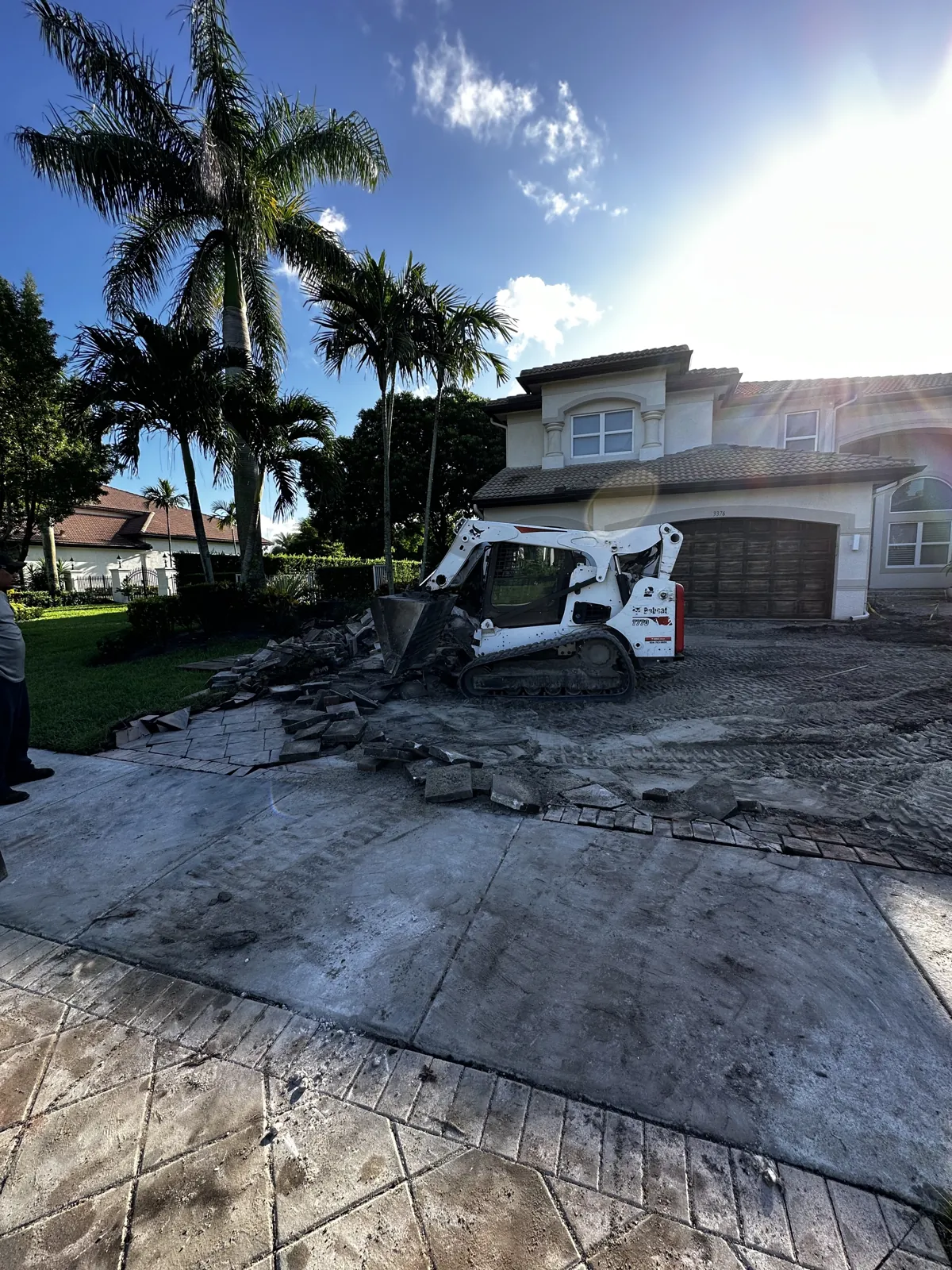 Old driveway surface being removed with a skid steer in front of a two-story home