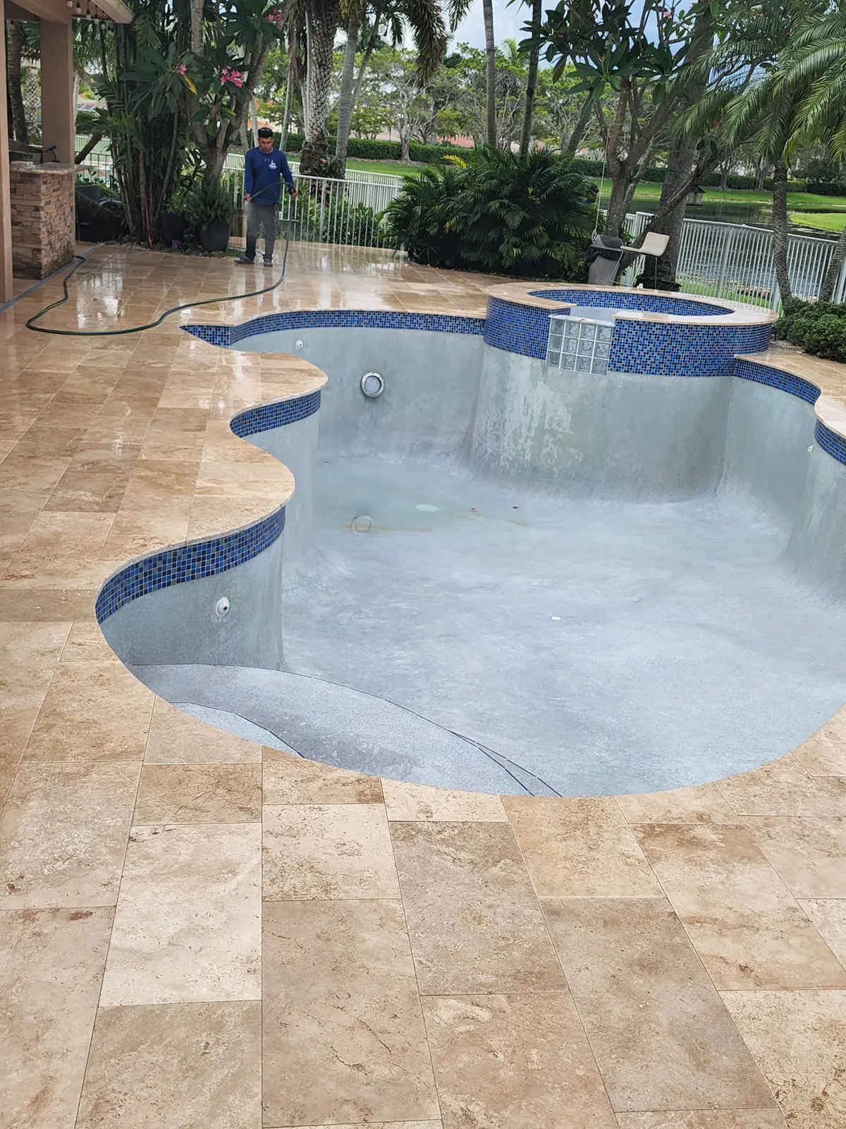 Completed travertine deck around a drained freeform pool with blue tile