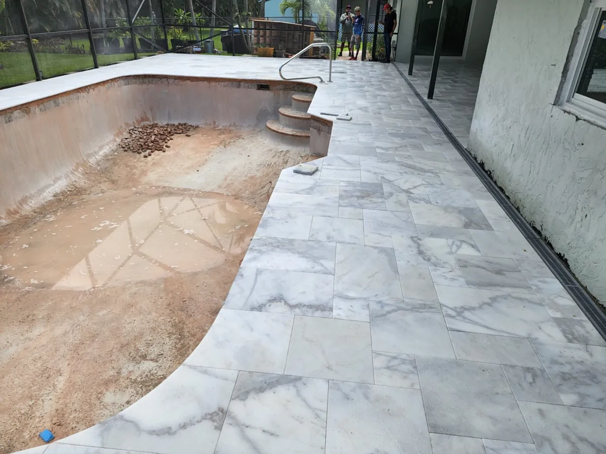 Marble-look tile deck laid beside a drained pool