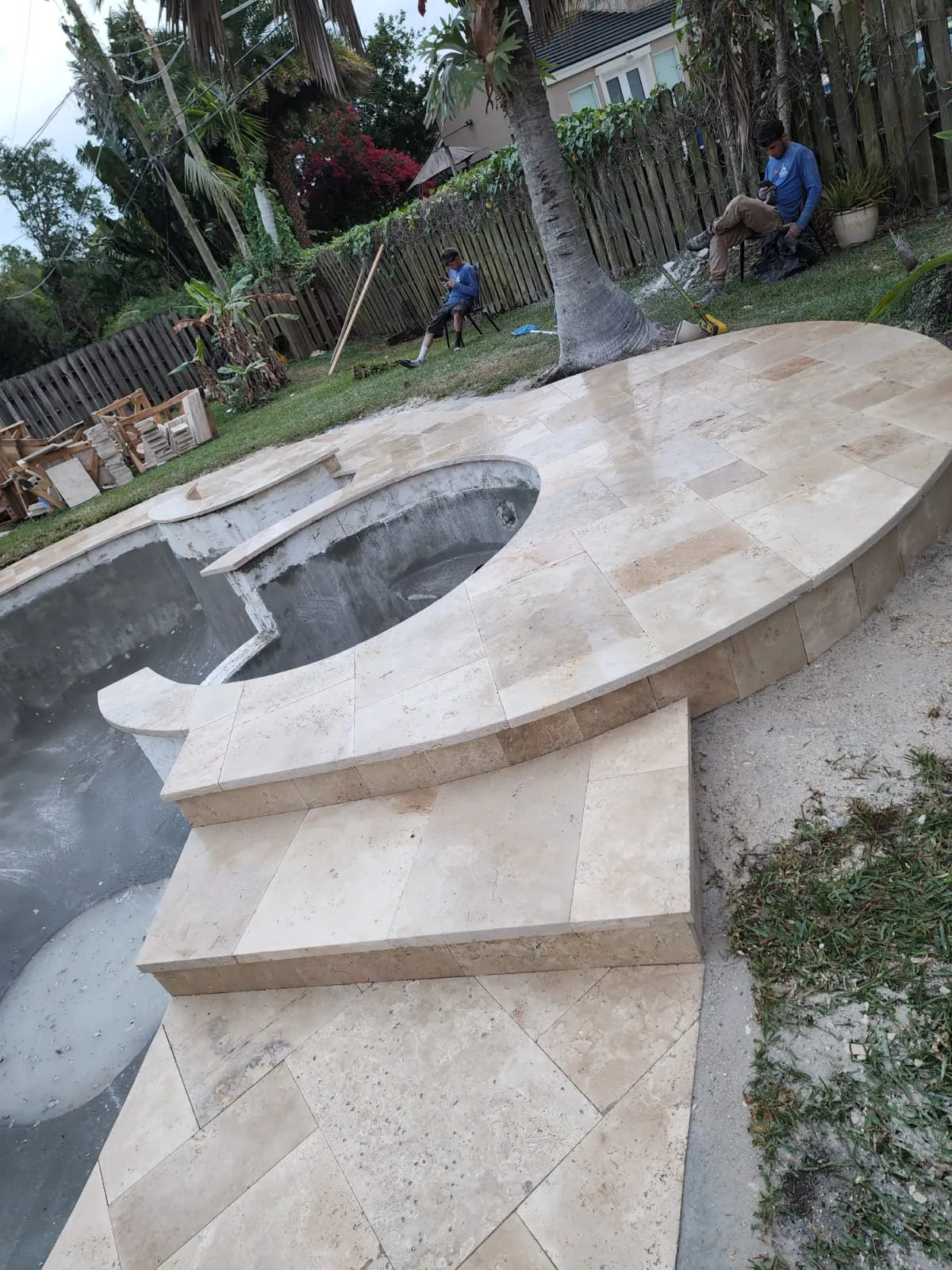 Travertine coping set around a round spa beside a pool under renovation